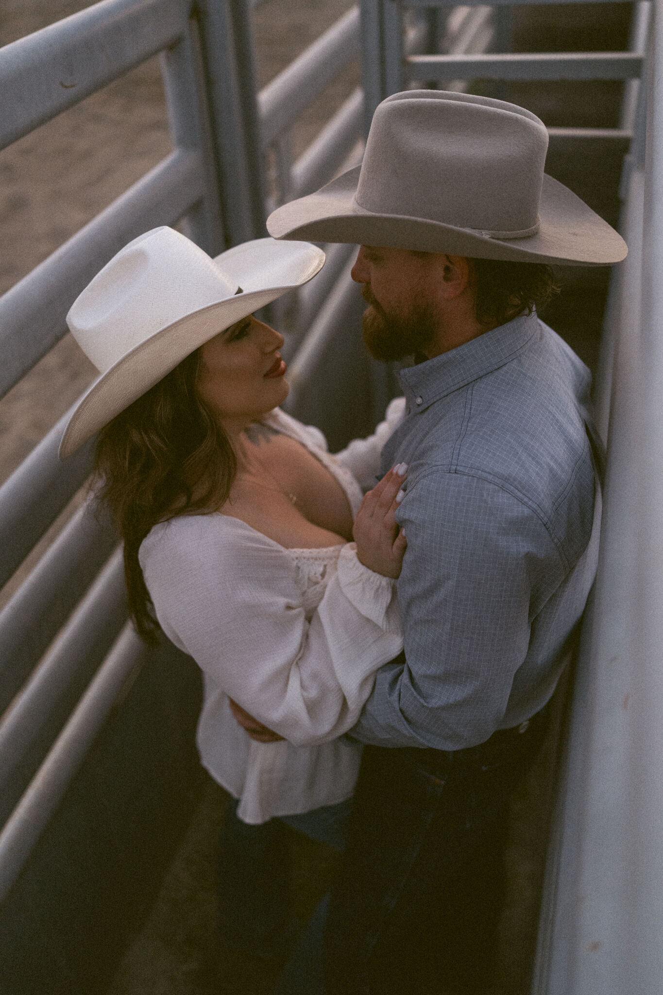 Couple embracing between the rails of a rodeo arena at dusk