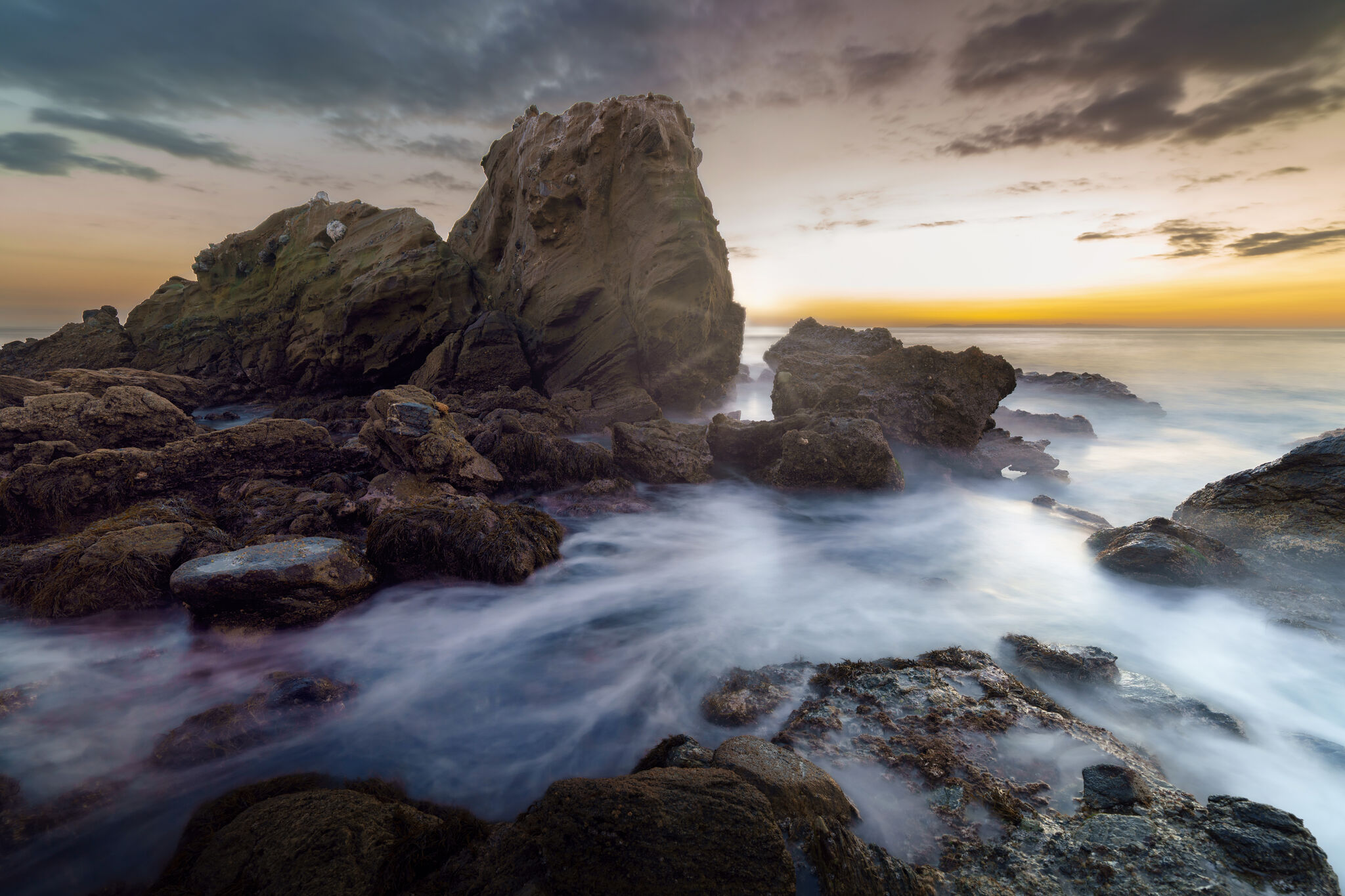 Waves washing over dark rocks at sunset on the California coast